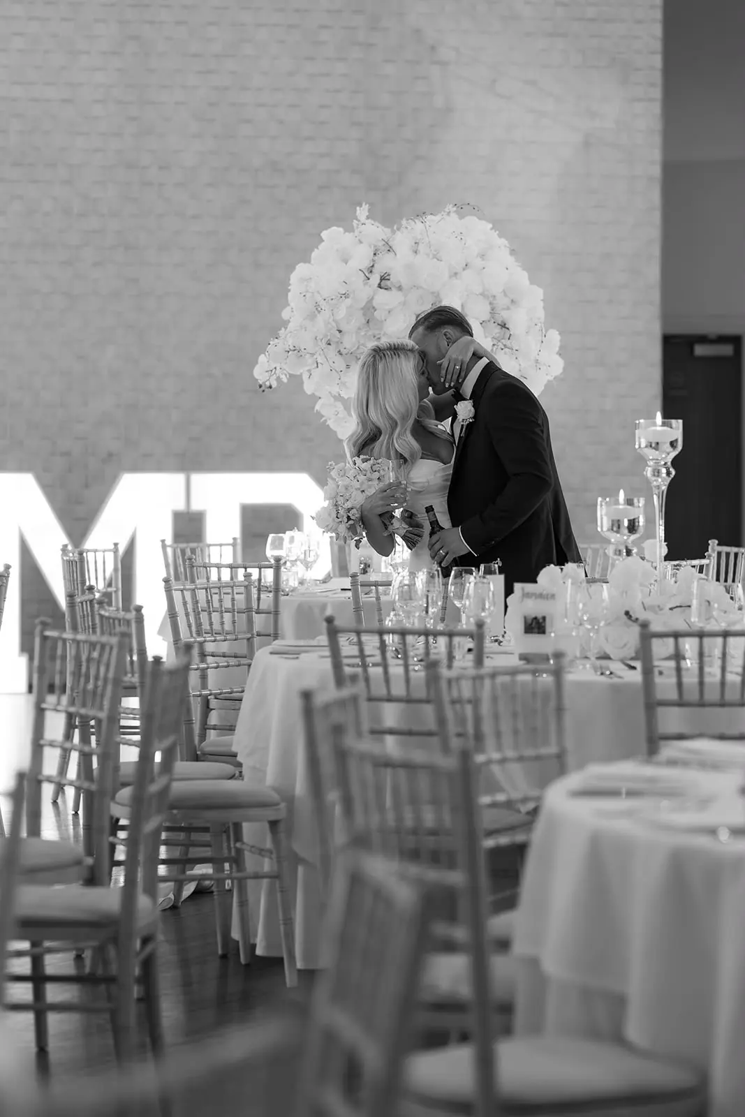 Bride and groom kissing in front of illuminated MR & MRS letters at their reception